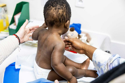 Bébé assis sur une table, tenu par deux mains de deux personnes, la mère et le professionnel de la santé