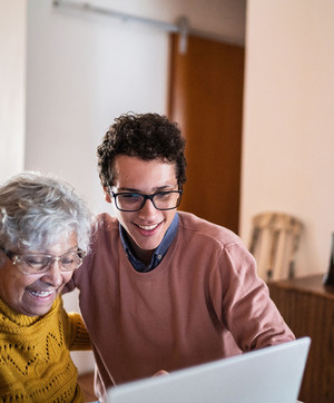 Jeune homme aux c&ocirc;t&eacute; d'une dame &acirc;g&eacute;e, les deux regardant un ordinateur et riants