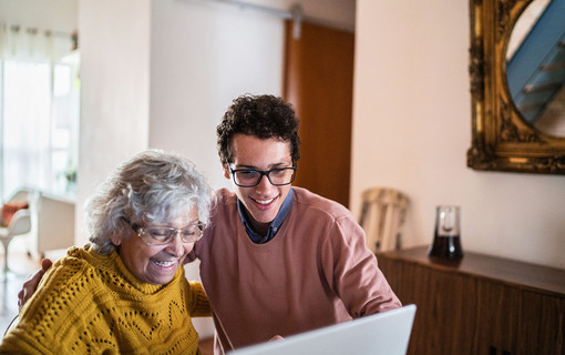 Jeune homme aux c&ocirc;t&eacute; d'une dame &acirc;g&eacute;e, les deux regardant un ordinateur et riants