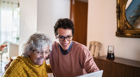 Jeune homme aux c&ocirc;t&eacute; d'une dame &acirc;g&eacute;e, les deux regardant un ordinateur et riants