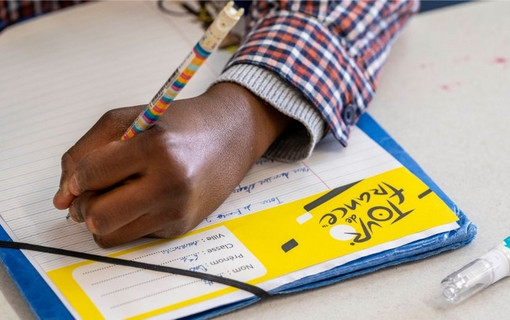 Gros plan d'une main de collégien écrivant sur une copie à en-tête Dictée du Tour